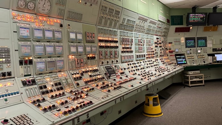 Control panels with many lights, knobs, switches, dials and screens, in the control room of a nuclear power plant. 