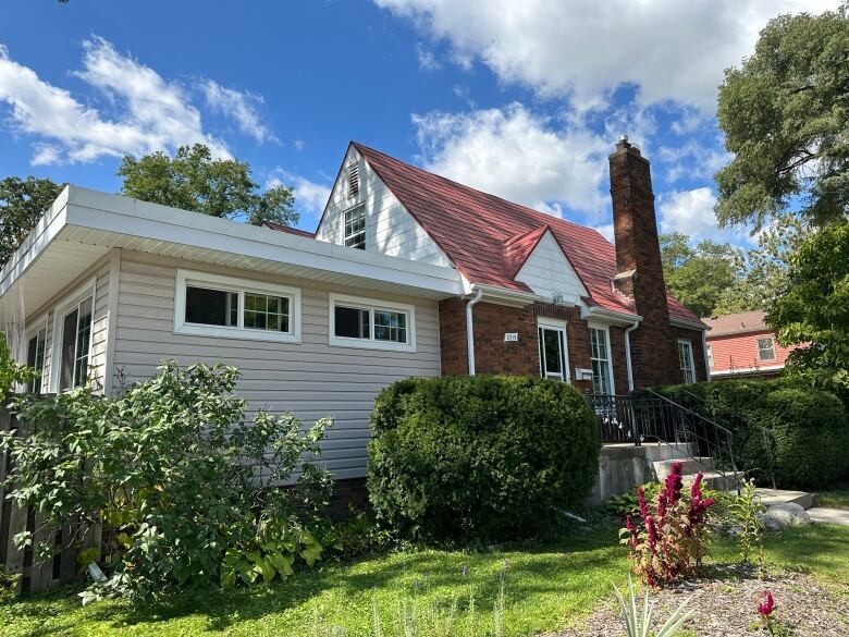 A picture of a brown brick home, with a red shingled roof and chimney stack. 