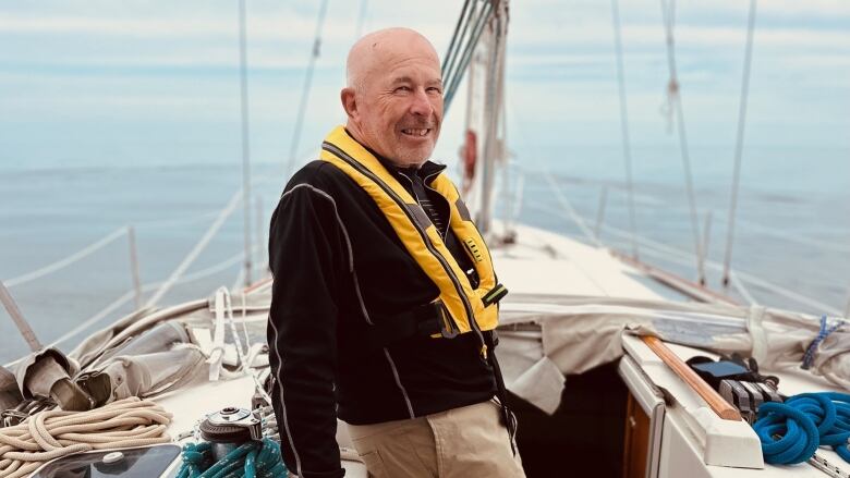 A smiling older gentleman stands on the deck of a sailboat.