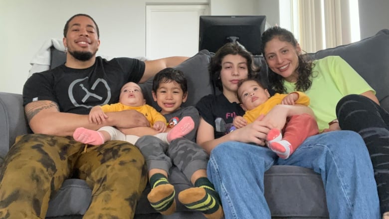 A mother, father and their four children smile for the camera on a grey couch.