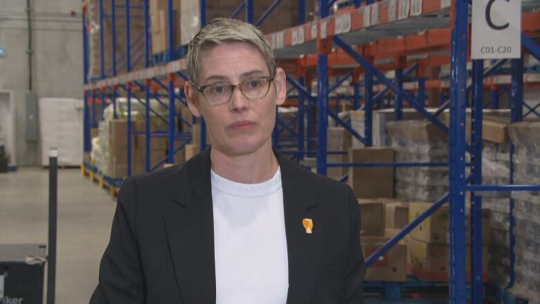 A woman stands in a warehouse in front of industrial metal shelving full of boxes.