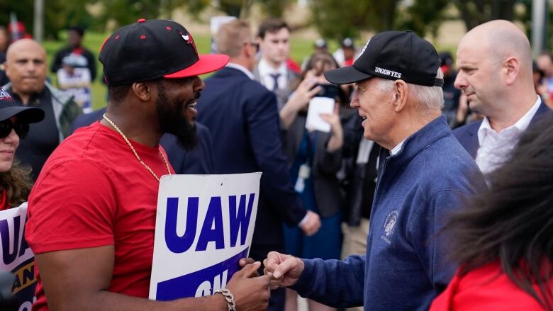 U.S. President Joe Biden, wearing a blue sweater and a black ball cap emblazoned with the words 'union yes,' bumps fists with a man in a red t-shirt and a Chicago Bulls hat holding a United Auto Workers sign. 