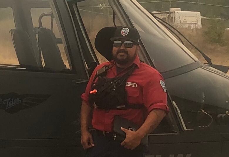 A man poses in front of a helicopter on a smokey day