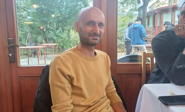 A thin man in a yellow shirt sits at a table.