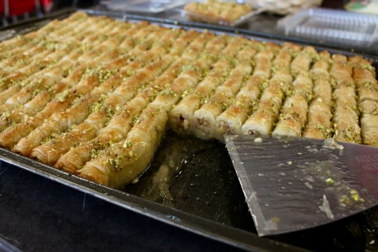 A tray of tiny, golden, flaky patries drenched in syrup and topped with nuts.