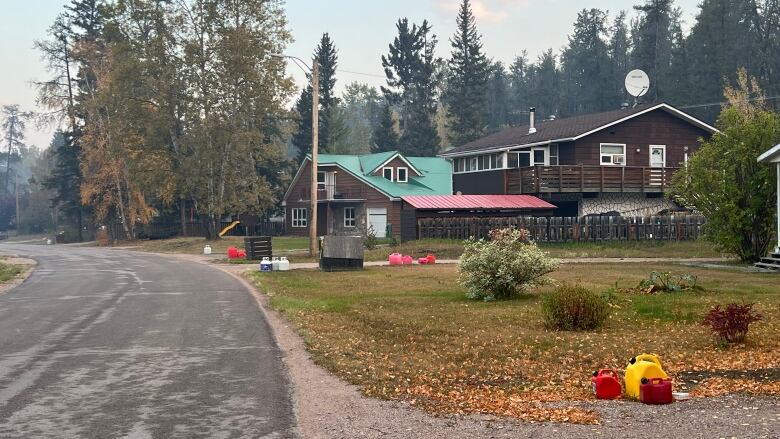 Jerry cans of gas sit on a roadside, near homes. Smoke hangs in the air.