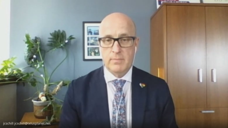 Jason Schilling, president of the Alberta Teachers Association, participates in an online interview. He wears a blue suit and wears white earbuds.