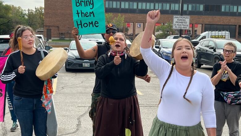 People stand in a parking lot chanting and drumming.