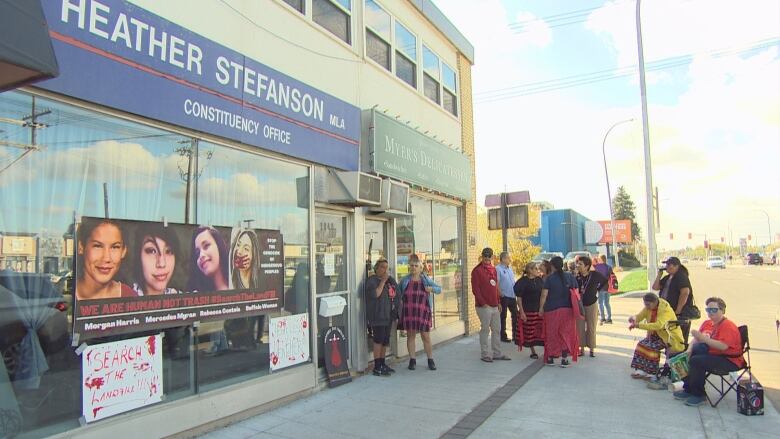 People stand outside a building. Signs that say 