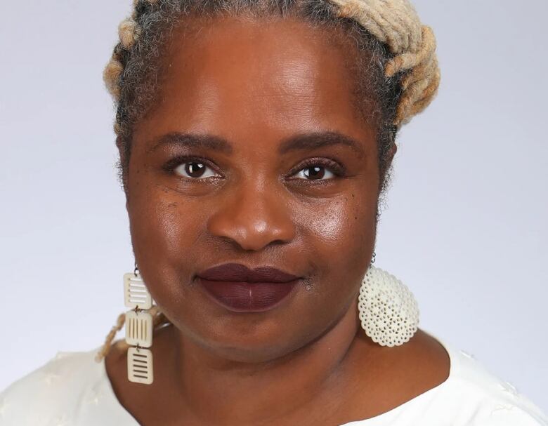 A woman wearing a white shirt and long silver earrings smiles into camera. 