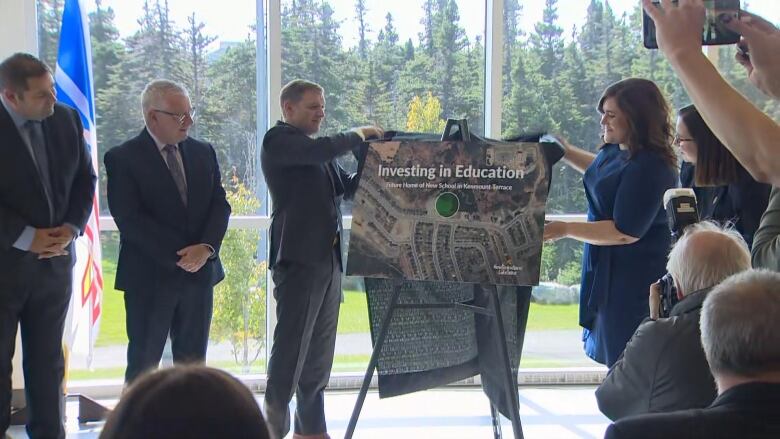 People in suits gather around a board, pulling cloth from it.