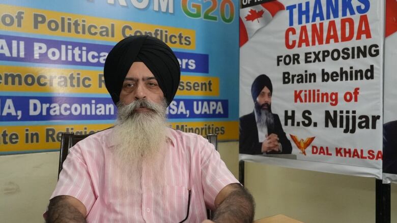 A person sits in a chair in front of a wall with posters on it.