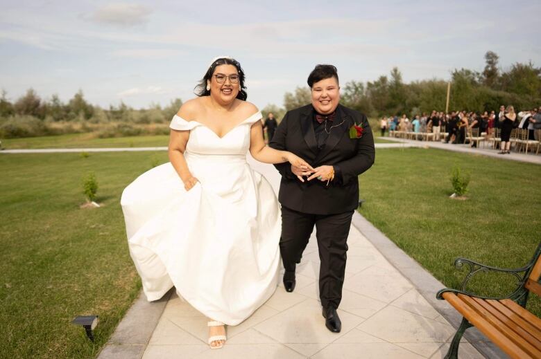 Newly couple hold hands. There is family, friends and allies in the background