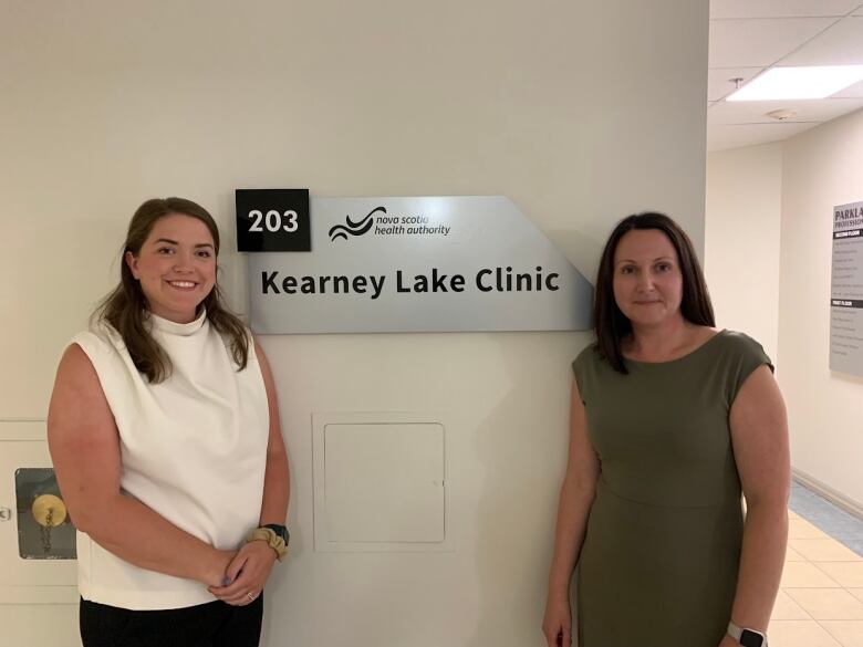 Two woman stand between a silver sign that reads Nova Scotia Health Authority Kearney Lake Clinic.