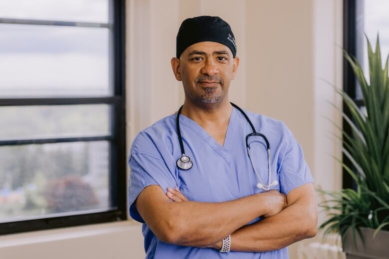 Man wearing scrubs and a stethoscope stands with his arms crossed.