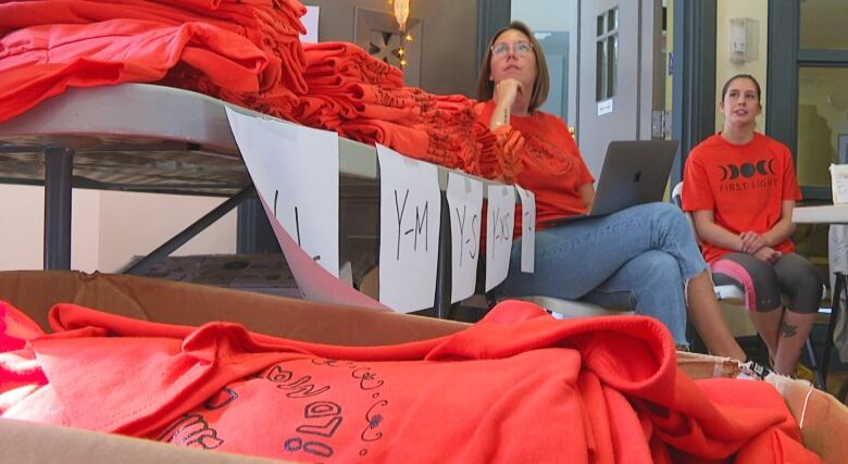 Woman sit behind boxes of orange shirts