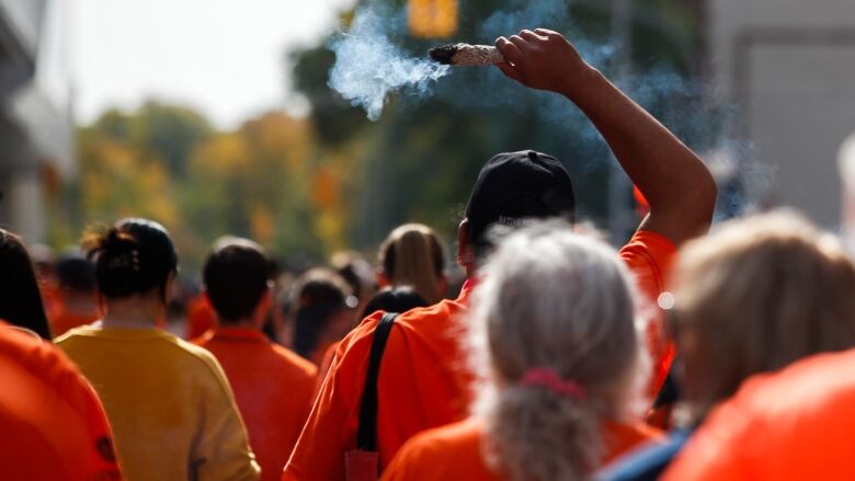 A crowd of marchers are pictured from behind. A man is shown in the middle holding a bundle of burning sage.