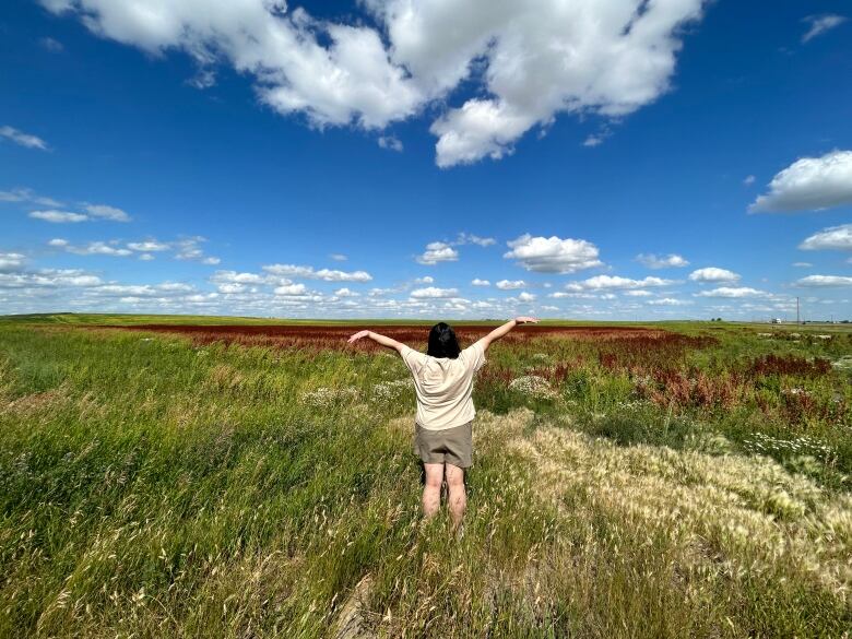 A young woman stands in a prairie field. 