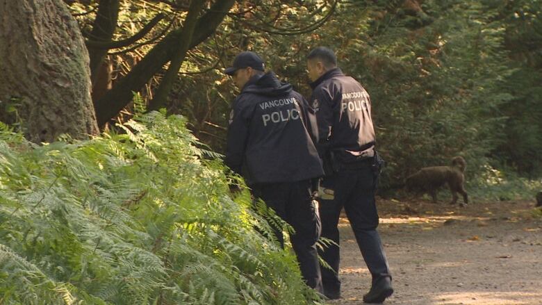 Two police officers look at a bush in a park.