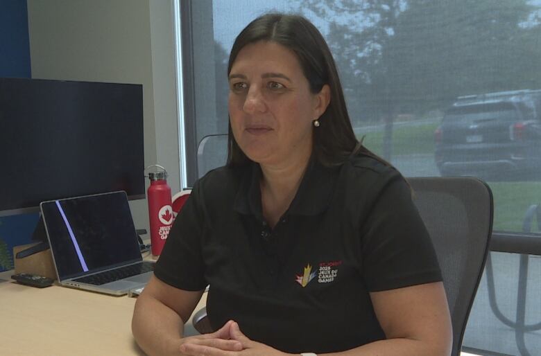 A woman is pictured inside her office. She is wearing a Canada Games shirt. 