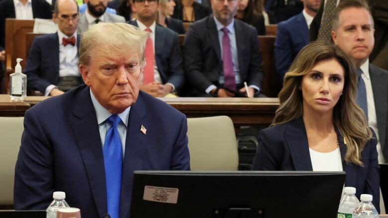 A man in a suit and tie sits at a table beside a woman in a blazer.