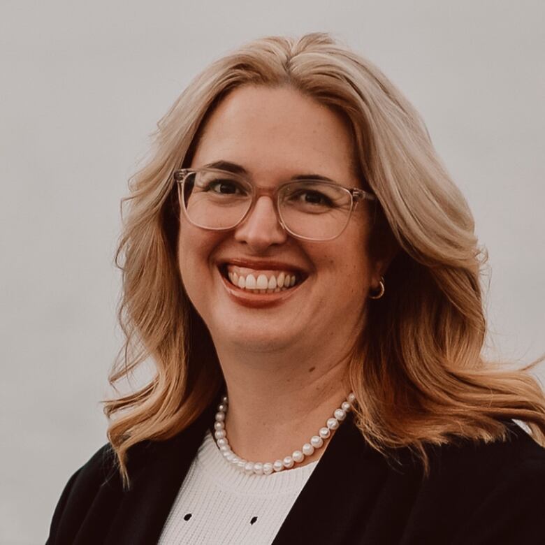 A woman with blonde hair and glasses. She is smiling.