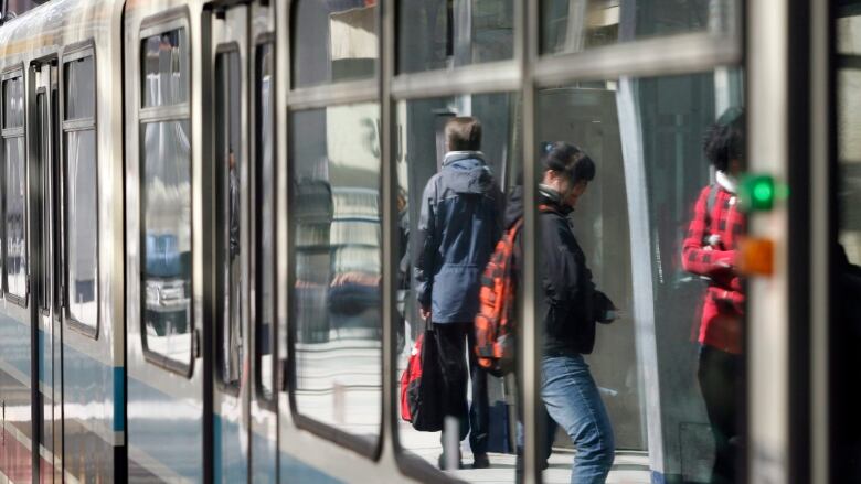 People are seen in the reflection of C-Train windows.