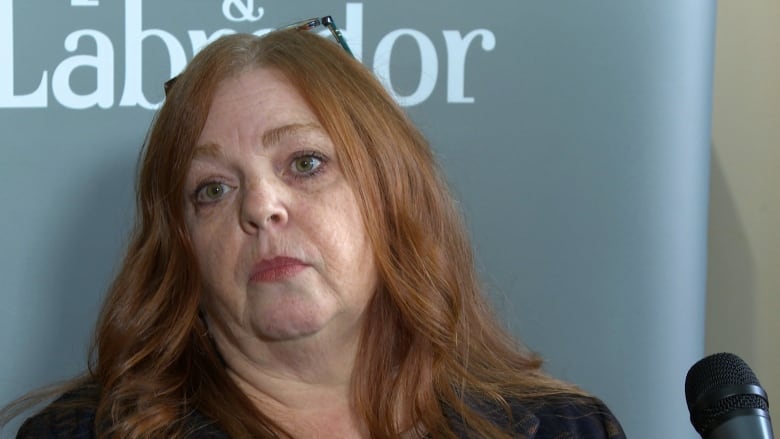 A woman with long red hair stands in front of a microphone.