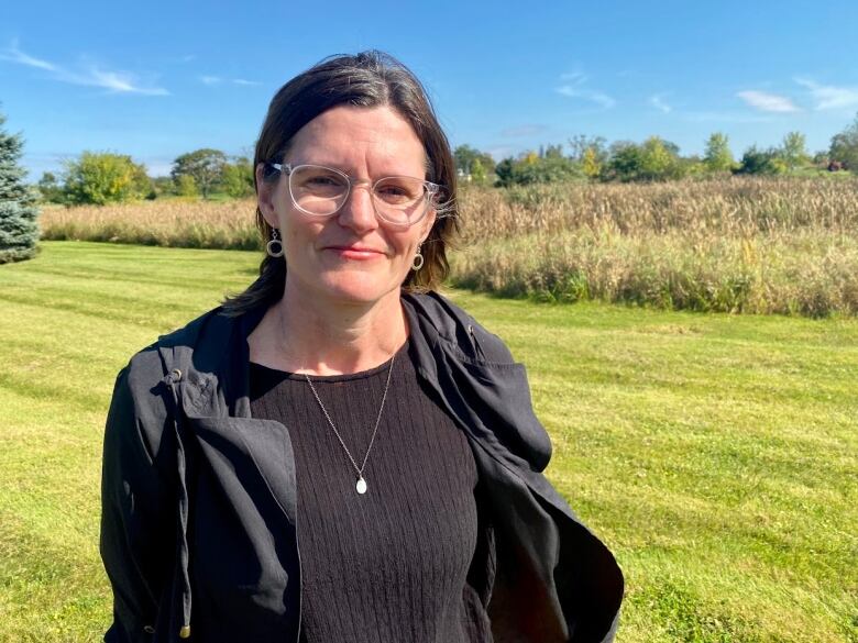 A woman stands in front of a field on a sunny day. 