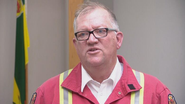 A man in a red work jump suit wears glasses.