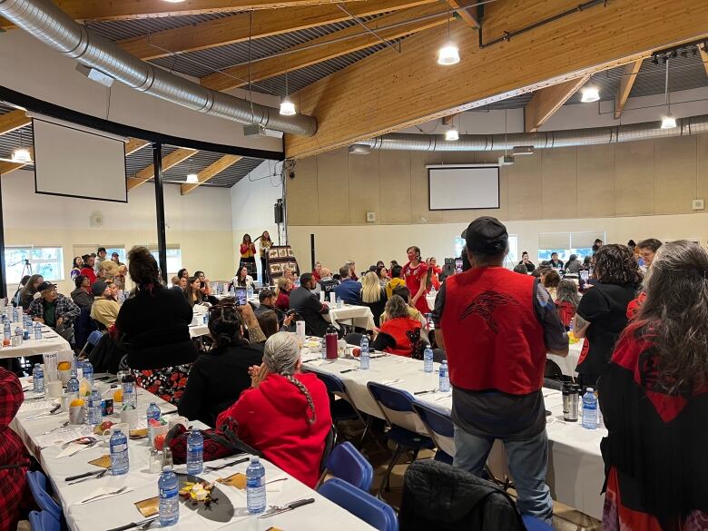 People dressed in red, standing and clapping at long dining tables. 