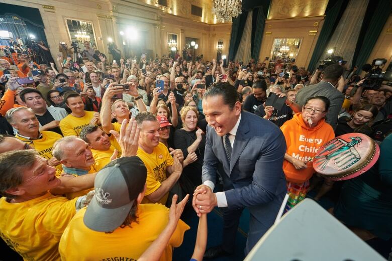 A man in a suit is surrounded by a throng of people in a hotel ballroom.