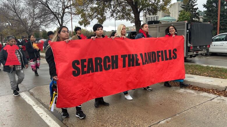 Five marchers carry a large red banner that says 