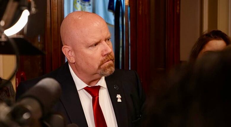 Serious-looking man in a dark suit in the centre of a media scrum.