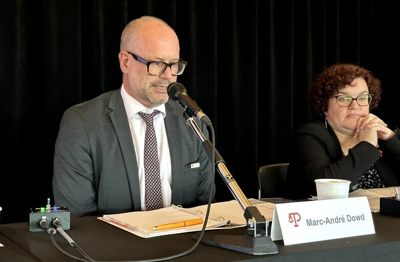 A man in a suit speaks into a microphone. 