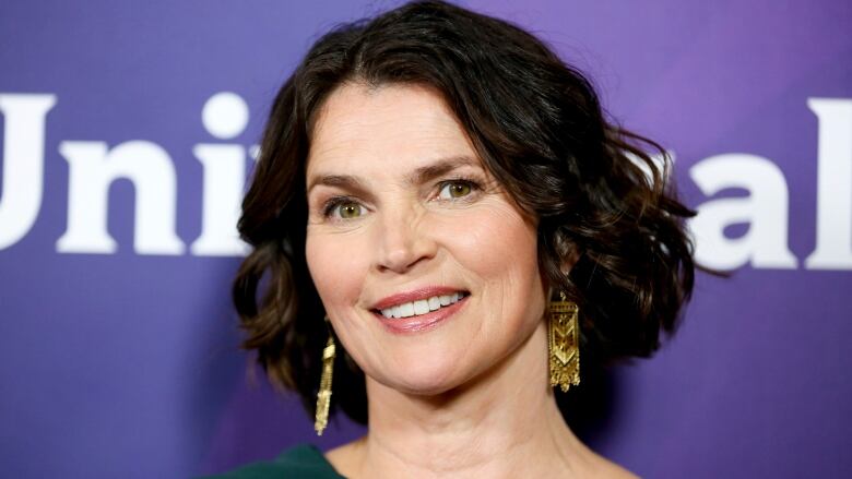 A woman with short dark hair and gold earrings smiles during an event.