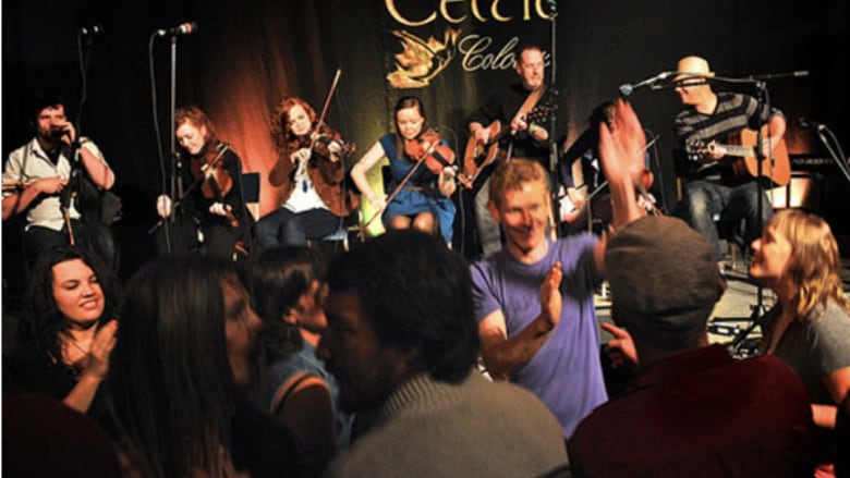  People dancing in front a of a large stage where musicians are playing. There is a sign that says Celtic Colours in the background.