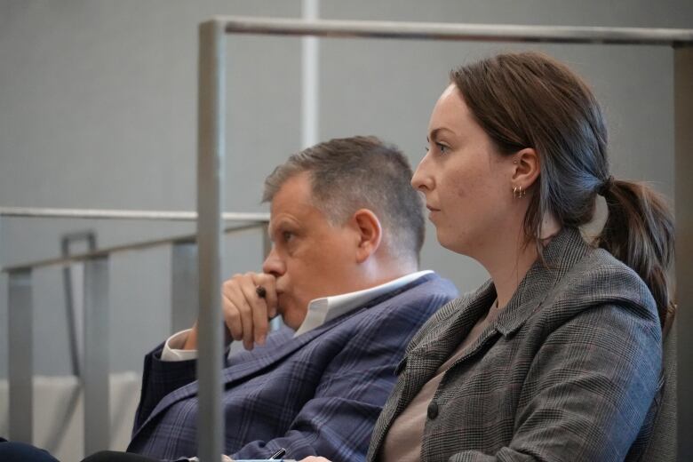 Two people sitting in chairs listening to people speak