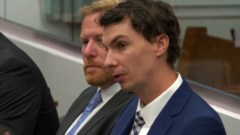 Two men wearing suits look off camera during a government committee meeting. 