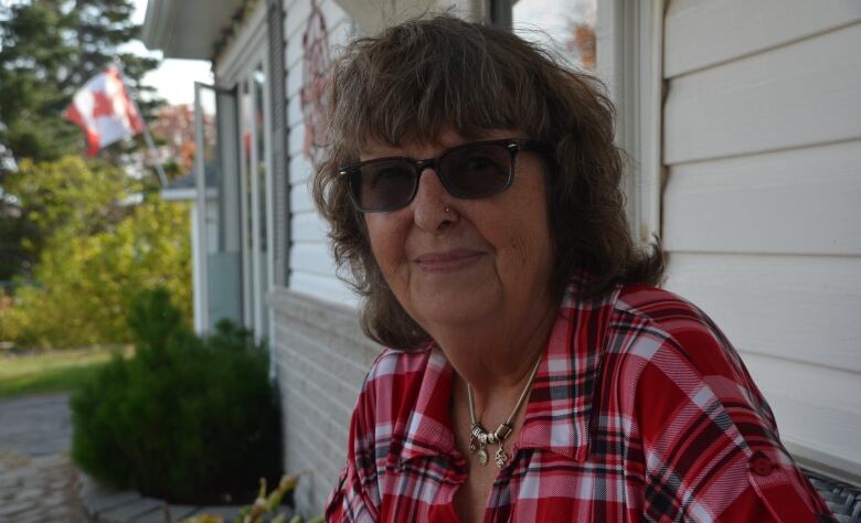 A woman wearing sunglasses and a plaid shirt sits on a porch