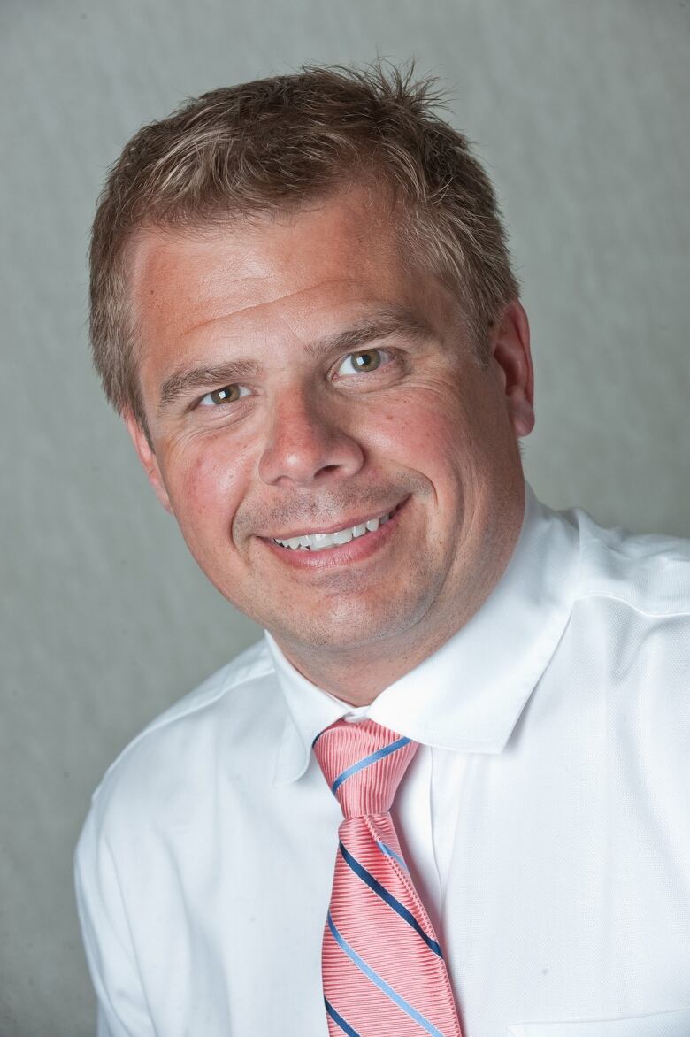 A man wears a white button-up blouse with a pink tie.