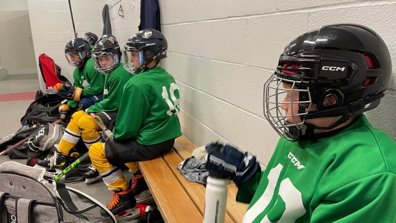 Young hockey players sit on a bench in a dressing room.