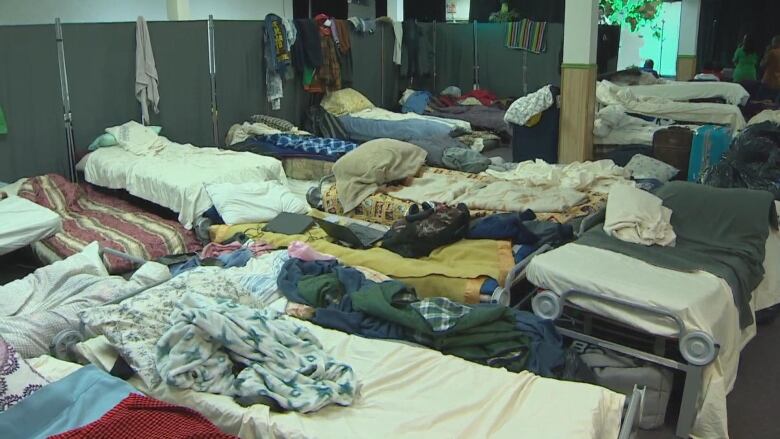 Empty cots with blankets and other belongings are pictured inside a room.