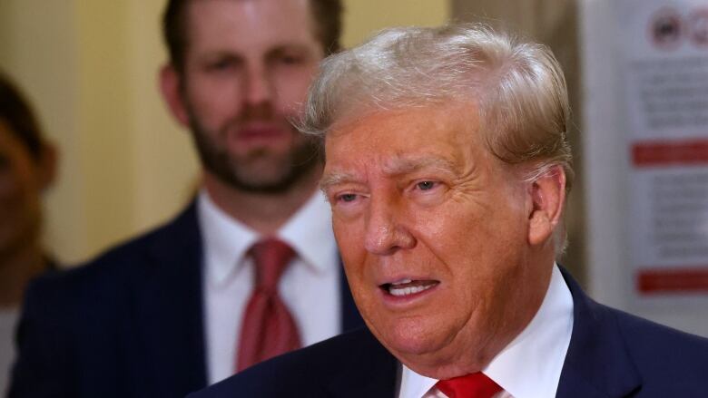 Former U.S. president Donald Trump speaks to the media, with his son Eric Trump standing behind him.