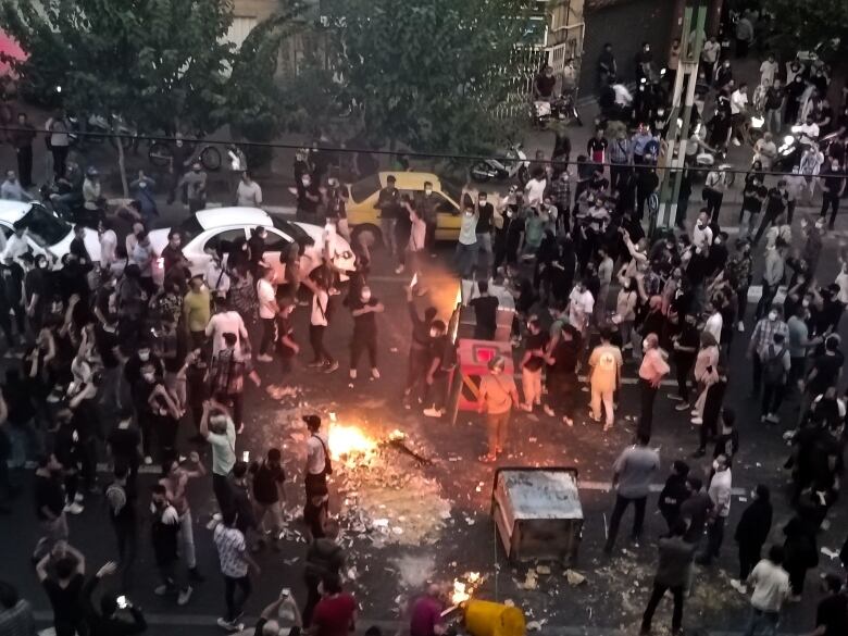 An overhead view shows dozens of demonstrators and vehicles at an intersection, with a bonfire in the middle of the street shown.