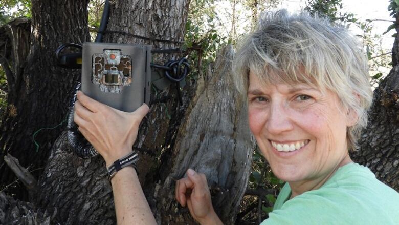 Woman stands beside a tree fitted with video recording equipment