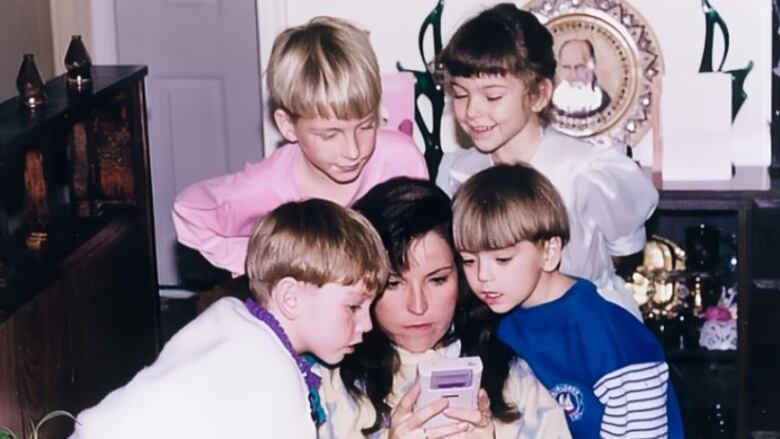 Four kids huddle around a mother playing a game boy.