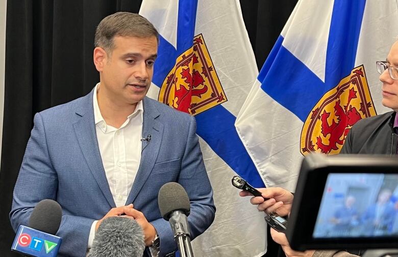 A man in a blue blazer and white shirt sands in front of reporters holding microphones.