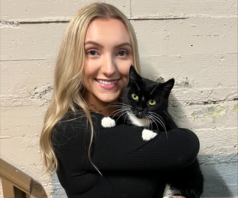 A woman with blonde hair holding a cat next to a concrete wall. 