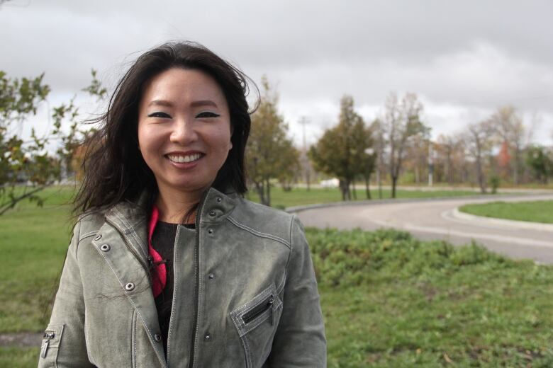 A woman with dark brown hair stands on a lawn next to a road.